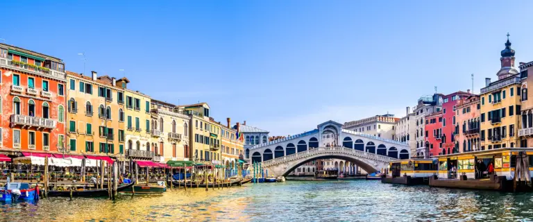 Rialto Bridge spanning the Grand Canal between colorful historic buildings in Venice.