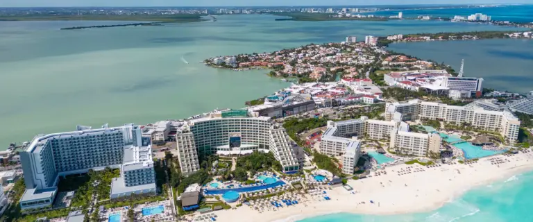 Aerial view of Cancun’s hotel zone between turquoise Caribbean water, white-sand beaches, and the Nichupté Lagoon.