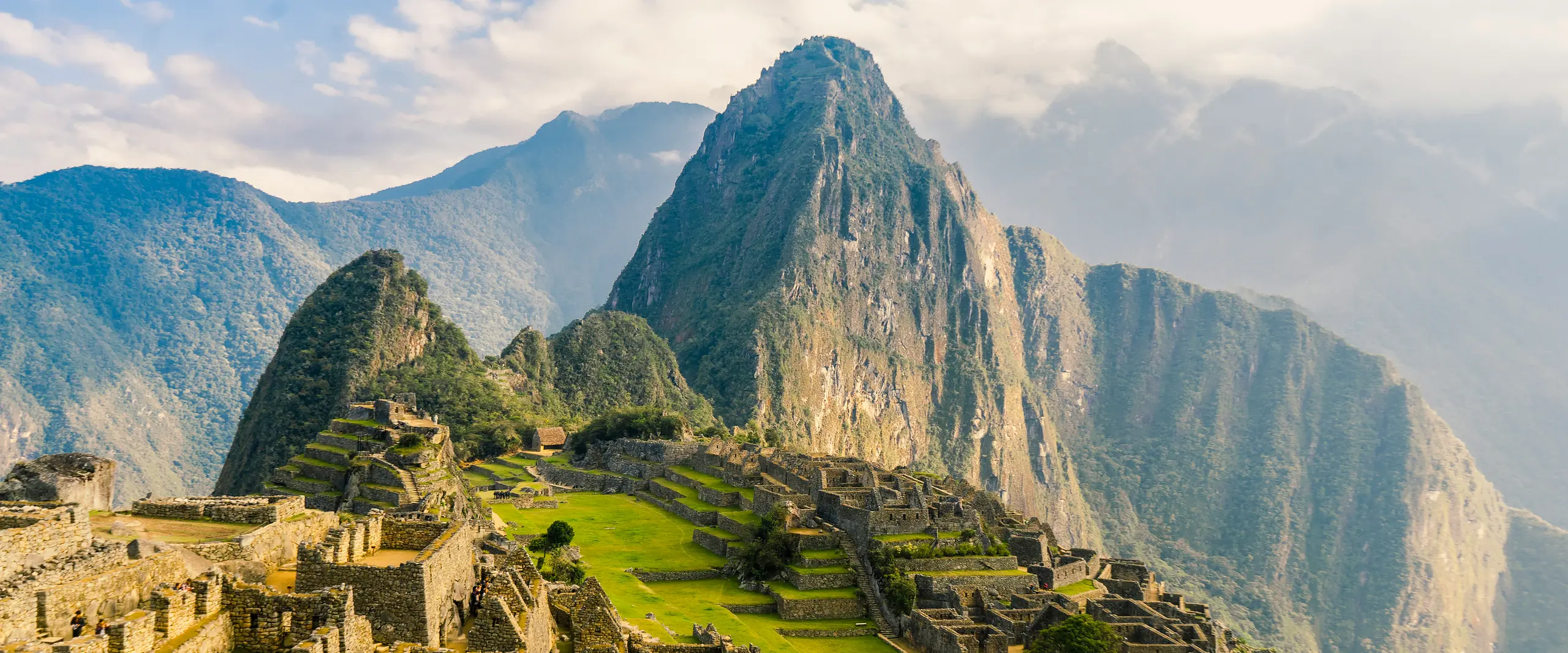 Machu Picchu stone ruins and green terraces beneath Huayna Picchu in warm morning light.