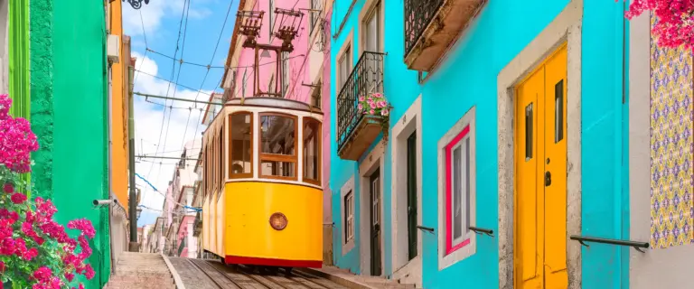 Funicular amarelo da Bica em uma rua íngreme cercada por casas coloridas e flores em Lisboa.